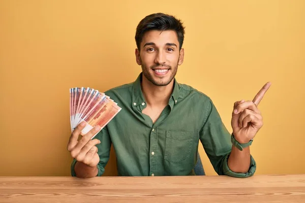 Joven Hombre Guapo Sosteniendo Billetes Noruegos Sonriendo Feliz Señalando Con —  Fotos de Stock