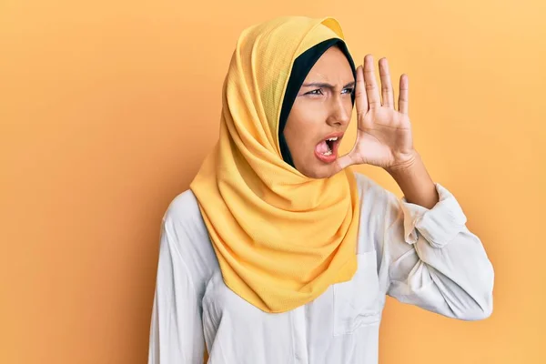 伝統的なイスラム教のヒジャーブスカーフを身に着けている若いブルネットのアラブ女性は大声で叫び 口の中で手で横に大声で叫ぶ コミュニケーションの概念 — ストック写真