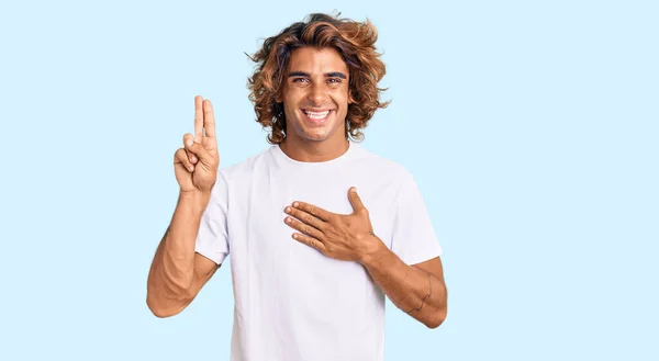 胸と指で手で身に着けて笑顔のカジュアルな白いTシャツを着た若いヒスパニック系の男 忠誠の誓いを作る — ストック写真