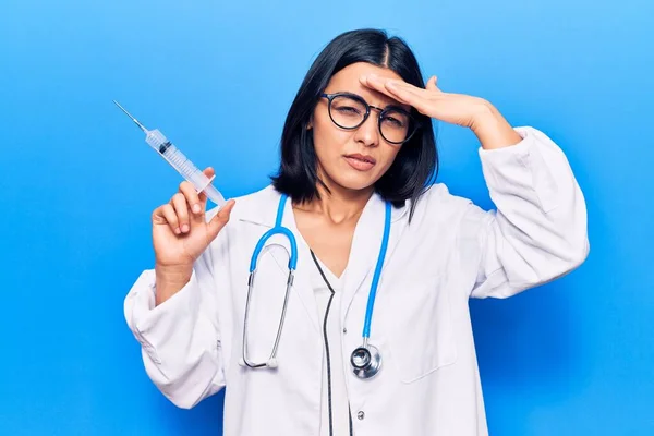 Young beautiful latin woman wearing doctor stethoscope holding syringe stressed and frustrated with hand on head, surprised and angry face