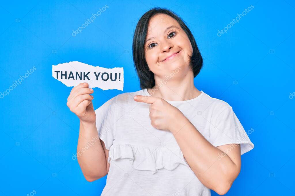 Brunette woman with down syndrome holding thank you paper smiling happy pointing with hand and finger 