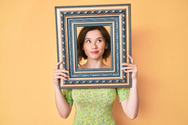 Genç, güzel bir kadın boş bir çerçeve tutuyor gülümsüyor, yan tarafa bakıyor ve düşünüyor.. 