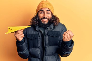 Kâğıt uçak tutan genç Arap adam gururla haykırıyor, zaferi ve başarıyı kutluyor. 