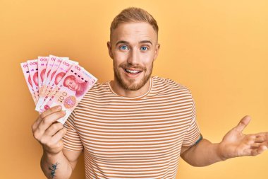 Kafkasyalı genç adam 100 Yuan Çin banknotları tutuyor başarıyı mutlu bir gülümsemeyle kutluyor ve kazanan el kaldırarak ifade ediyor 