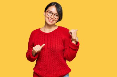 Kısa saçlı, sıradan bir süveter giyen ve gözlüklü genç, güzel bir İspanyol kadın. Arka tarafı işaret ediyor. El ve baş parmakları havada, kendinden emin. 