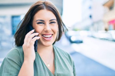 Genç İspanyol kadın gülümsüyor. Şehrin caddesinde yürüyen akıllı telefonla konuşuyor.