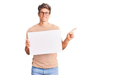 Boş afiş tutan genç yakışıklı adam gülümsüyor mutlu bir şekilde eli ve parmağı yana doğru işaret ediyor. 