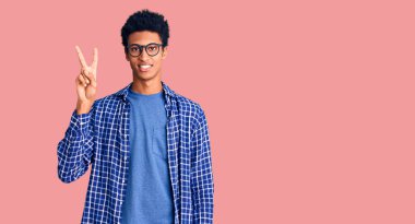 Genç Afro-Amerikan adam günlük kıyafetler ve gözlük takıyor ve parmaklarını iki numara ile gösteriyor ve gülümsüyor kendinden emin ve mutlu.. 