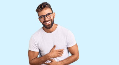 Gündelik kıyafetler ve gözlük takan genç İspanyol adam gülümseyerek ve kahkahalarla gülüyor çünkü elleri vücutta olan komik çılgın bir şaka.. 