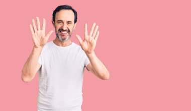 Orta yaşlı yakışıklı bir adam gündelik tişört giyer ve parmaklarıyla on numarayı gösterirken kendinden emin ve mutlu bir şekilde gülümserdi.. 