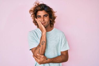 Günlük kıyafetler giyen genç İspanyol adam kollarını kavuşturarak depresyondan sıkılmış ve yorgun görünüyor.. 