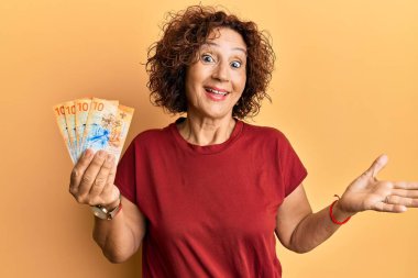 Güzel, orta yaşlı bir kadın elinde 10 İsviçre frangı banknotuyla başarıyı mutlu bir gülümsemeyle ve kazanan ifadeyle kutluyor. 