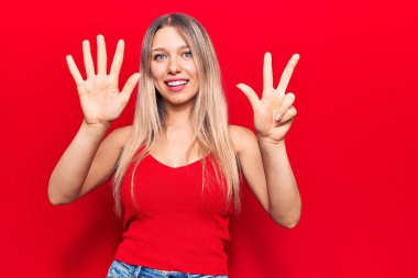 Gündelik kıyafetler giyen genç sarışın kadın sekiz numarayı gösterip işaret ederken kendinden emin ve mutlu bir şekilde gülümsüyor.. 