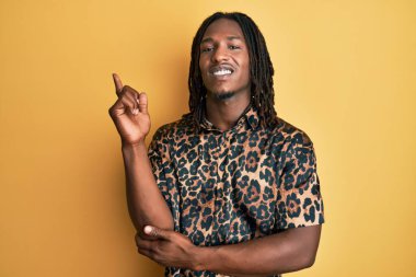 Saçları örgülü, leopar desenli, yüzünde kocaman bir gülümseme olan, elleri ve parmaklarıyla kameraya bakan Afro-Amerikan bir adam.. 
