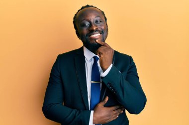 Yakışıklı, takım elbiseli ve kravatlı genç bir adam kameraya kollarını kavuşturmuş ve çenesi açık bir şekilde gülümsüyor. Olumlu düşünmek. 