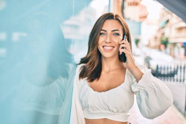 Genç İspanyol kadın gülümsüyor. Şehirdeki akıllı telefondan konuşuyor..
