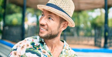 Yazlık şapkalı ve çiçekli tişörtlü yakışıklı beyaz adam dışarıda mutlu gülümsüyor.
