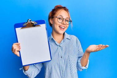 Genç kızıl saçlı kadın elinde boş bir panoyla başarıyı mutlu bir gülümsemeyle kutluyor ve kazanan el kaldırarak ifade ediyor. 