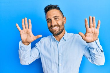 Sakallı, sıradan kıyafetler giyen yakışıklı bir adam on numarayı gösterip işaret ederken kendinden emin ve mutlu bir şekilde gülümsüyor.. 