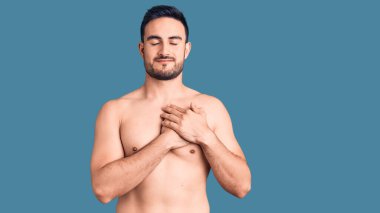 Mayo giyen, elleri göğsünde, gözleri kapalı gülümseyen ve yüzünde minnet ifadesi olan genç yakışıklı bir adam. sağlık kavramı. 