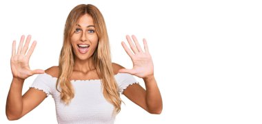 Güzel sarışın, beyaz tişört giyen genç bir kadın on numarayı gösterip işaret ederken kendinden emin ve mutlu gülümsüyor.. 