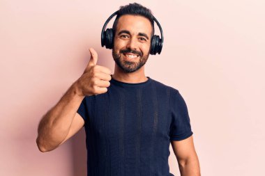 Genç İspanyol adam müzik dinliyor, kulaklık takıyor mutlu ve olumlu gülümsüyor, başparmağıyla mükemmel ve onay işareti yapıyor. 