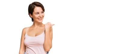 Kısa saçlı, kısa saçlı, yaz kıyafetleri giyen mutlu yüzüyle gülümseyen ve baş parmağıyla yüzünü gösteren genç esmer kadın.. 