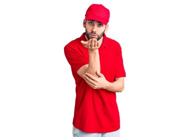 Genç, sakallı, teslimat üniforması giyen yakışıklı bir adam kameraya bakıp havada bir öpücük savuruyor ve sevimli ve seksi oluyor. aşk ifadesi. 