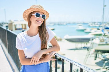 Genç sarışın kadın tatilde mutlu bir şekilde gülümsüyor. Kentin caddesinde korkuluklara yaslanıyor.