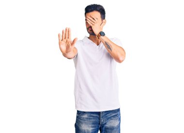 Genç, yakışıklı, günlük kıyafetler giyen, elleriyle gözlerini kapatan üzgün ve korku ifadeleriyle jestler yapan İspanyol bir adam. utangaç ve olumsuz kavram. 