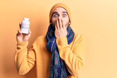 Sakallı, elinde hap şişesi olan genç ve yakışıklı bir adam ağzını eliyle kapatıyor. Şok geçiriyor ve hata yapmaktan korkuyor. şaşırmış ifade 