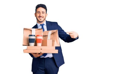 Takım elbiseli genç İspanyol adam elinde kahve ve yemek tutarken mutlu bir şekilde elini ve parmağını gösterdi. 