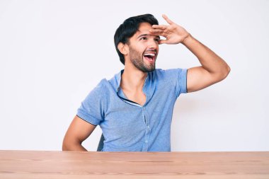 Yakışıklı İspanyol bir adam, gündelik giysiler içinde masada mutlu bir şekilde oturuyor ve gülümsüyor. arama kavramı. 