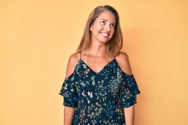 Orta yaşlı İspanyol kadın gündelik kıyafetler giyip yüzünde gülümsemeyle yan yana bakıyor, doğal bir ifade. Kendinden emin gülen. 