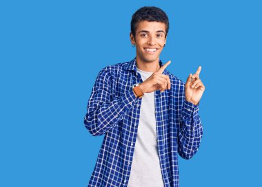 Genç Afrikalı Amerikalı sıradan kıyafetler giyen, gülümseyen ve kameraya bakıp iki elini ve parmağını yana doğru gösteren bir adam.. 