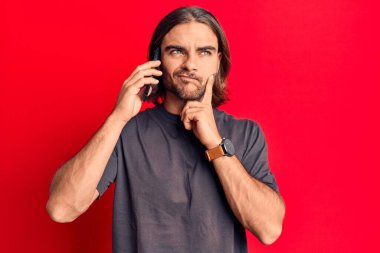 Genç yakışıklı bir adam akıllı telefondan konuşuyor ciddi bir yüz ifadesi, eli çeneli soruyu düşünüyor, kafa karıştırıcı bir fikir hakkında düşünceli. 