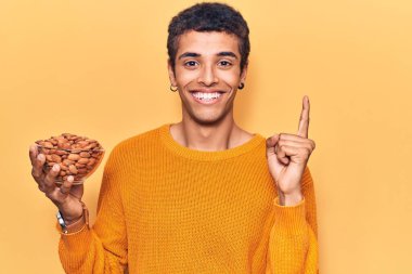 Genç Afrikalı Amerikalı elinde bademlerle gülümseyen bir adam bir fikir veya soru işareti ile mutlu bir yüzle, bir numara 