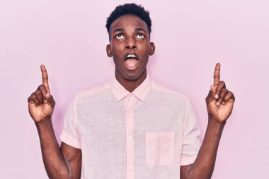 Gündelik giysiler giyen genç Afro-Amerikan adam şaşkın ve şaşırmış bir şekilde yukarı baktı ve parmaklarıyla işaret etti ve kollarını kaldırdı.. 