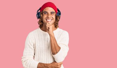 Genç İspanyol adam müzik dinliyor kulaklık takıyor kameraya özgüvenli bakıyor kollarını kavuşturup gülümseyerek ve çenesini kaldırarak. Olumlu düşünmek. 