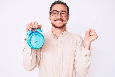 Genç yakışıklı adam çalar saati tutuyor gururla bağırıyor zaferi kutluyor ve başarıyı kollarını kaldırarak kutluyor. 