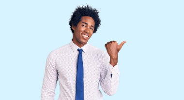 Afro saçlı, iş kıyafetleri giymiş, gülümseyen, gülümseyen ve baş parmağıyla yüzünü gösteren yakışıklı Afro-Amerikalı bir adam.. 