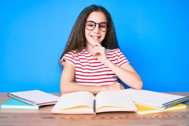 Tatlı İspanyol kız okul sınavına hazırlanıyor masaya oturmuş gülümsüyor ve elleri çapraz ve çenesinde kameraya bakıyor. Olumlu düşünmek. 