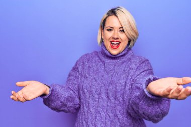 Güzel sarışın ve cüsseli bir kadın mor arka plan üzerine balıkçı yaka kazak giyip neşeli gülümseyerek yardım ve kabullenme eli uzatıyor..