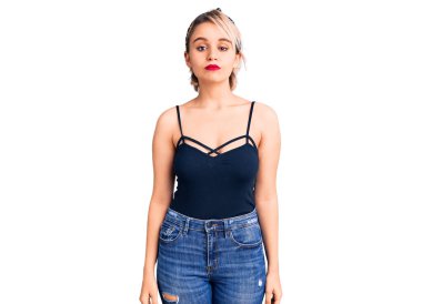 Yüzünde ciddi bir ifade olan sıradan kıyafetler giyen genç, güzel sarışın bir kadın. Basit ve doğal bir şekilde kameraya bakıyorsun.. 