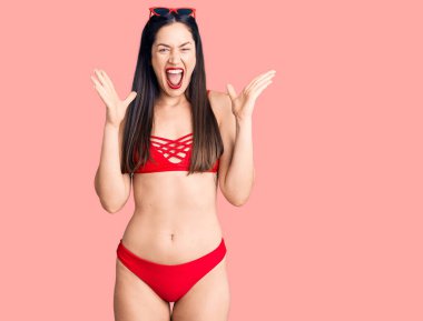 Genç beyaz kadın bikini giyip çılgınlığı kutluyor ve başarıya hayret ediyor kolları açık ve gözleri açık heyecanla haykırıyor. Kazanan konsept 