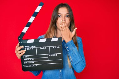 Güzel, beyaz bir kadın elinde video film panosu tutarak ağzını eliyle kapatmış, şok olmuş ve hata yapmaktan korkan. şaşırmış ifade 