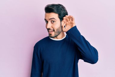 Gündelik kıyafetler giyen, ağzı kulaklarında gülümseyen, dedikoduları ve dedikoduları dinleyen genç İspanyol bir adam. Sağırlık kavramı. 