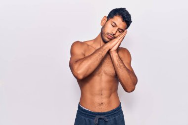 Genç latin adam üstsüz uyuyor. Yorgun düşler görüyor ve elleriyle poz veriyor. Gözleri kapalı gülümsüyor.. 