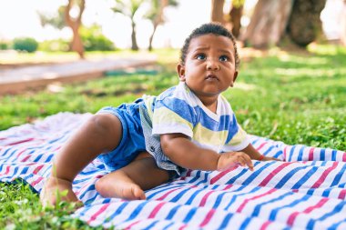 Sevimli Afro-Amerikan çocuk parkta çimlerin üzerinde oturuyor..