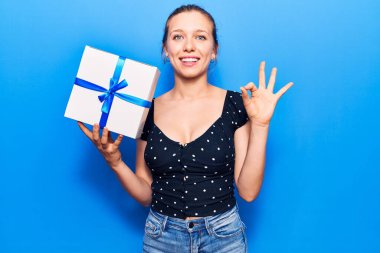 Sarışın genç kadın hediyesini tutuyor. Parmaklarıyla imza atıyor. Gülümsüyor. 